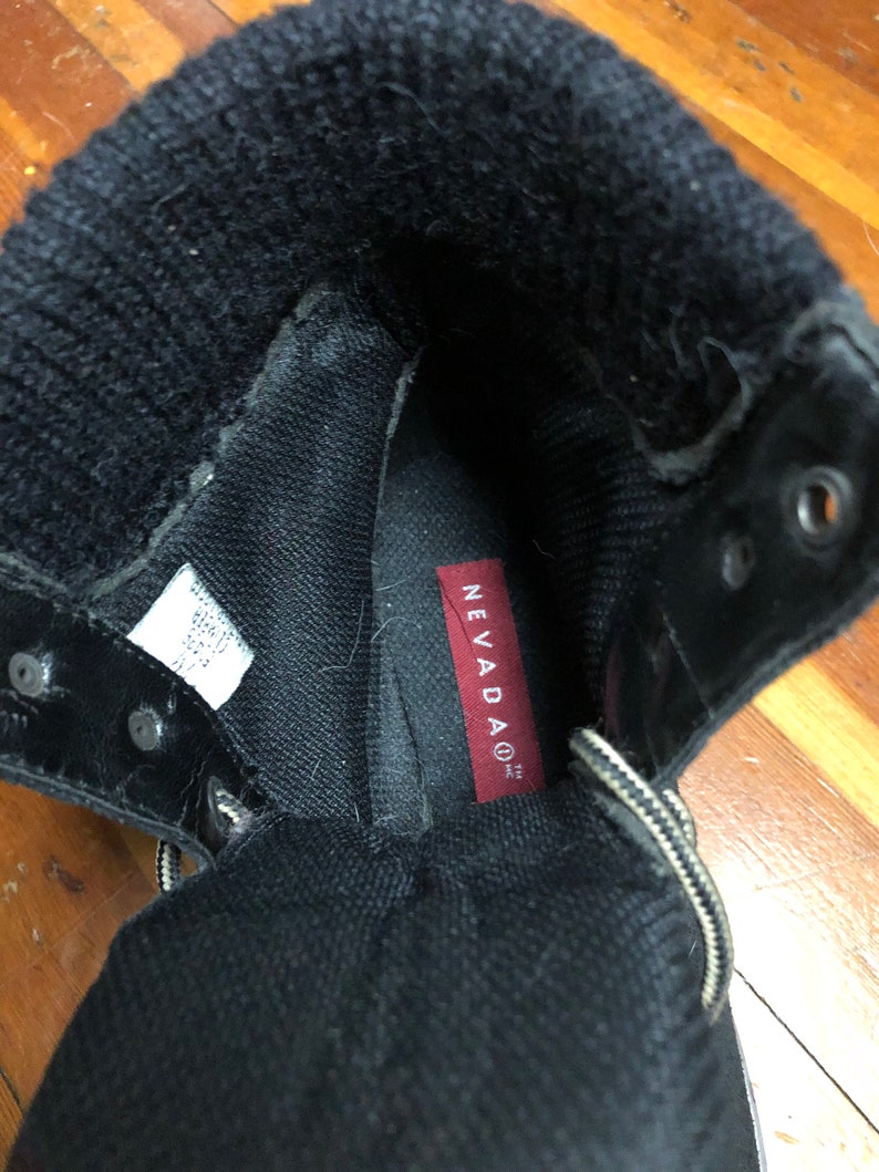 May include: Close-up of the inside of a black boot with a red label that says "NEVADAO TM INC".
