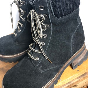 May include: Black suede ankle boots with a chunky platform sole and lace-up closure. The boots have a black knit cuff at the top.