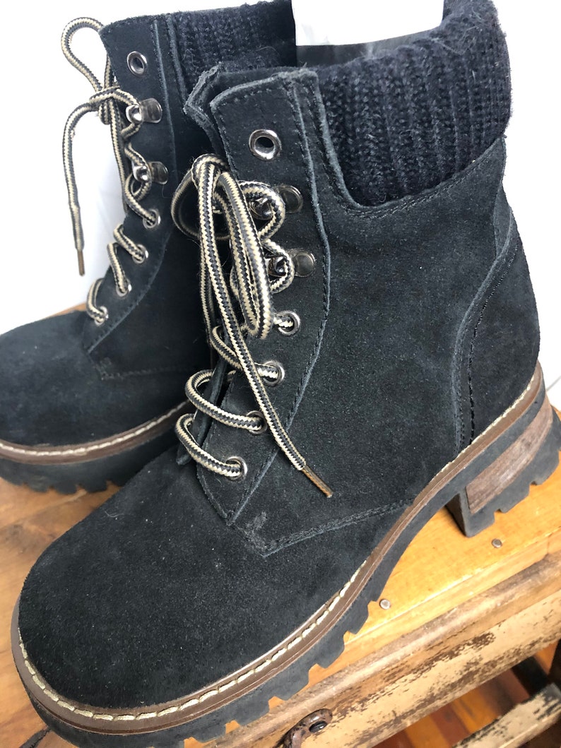 May include: Black suede ankle boots with a chunky platform sole and lace-up closure. The boots have a black knit cuff at the top.