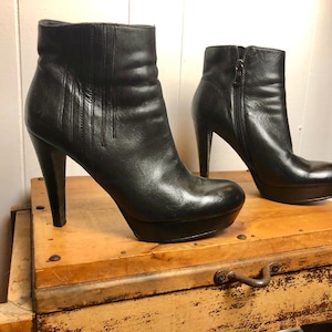 May include: A pair of black leather ankle boots with high heels and a platform. The boots have a zipper on the side and a pointed toe.