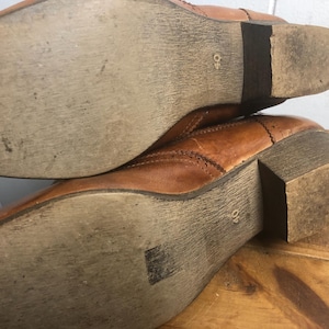 May include: Close-up of the soles of a pair of brown leather boots. The boots have a stitched design and a 40 size label on the sole.