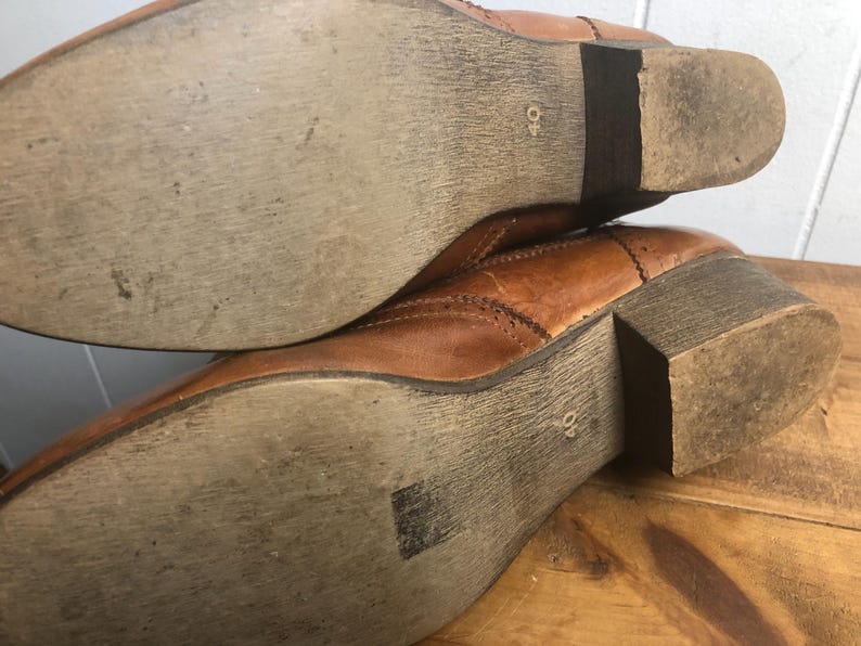 May include: Close-up of the soles of a pair of brown leather boots. The boots have a stitched design and a 40 size label on the sole.