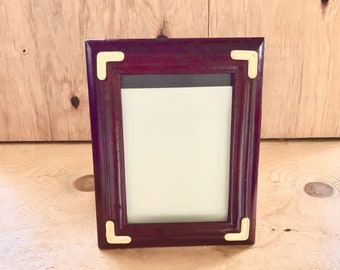 May include: A dark red wood picture frame with gold corner accents. The frame has a simple design and is ready to display a photo or artwork.