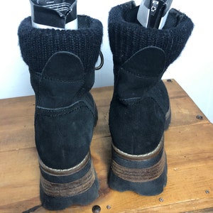 May include: Black suede ankle boots with a chunky platform sole and a knit cuff around the top. The boots have a brown leather trim around the sole.