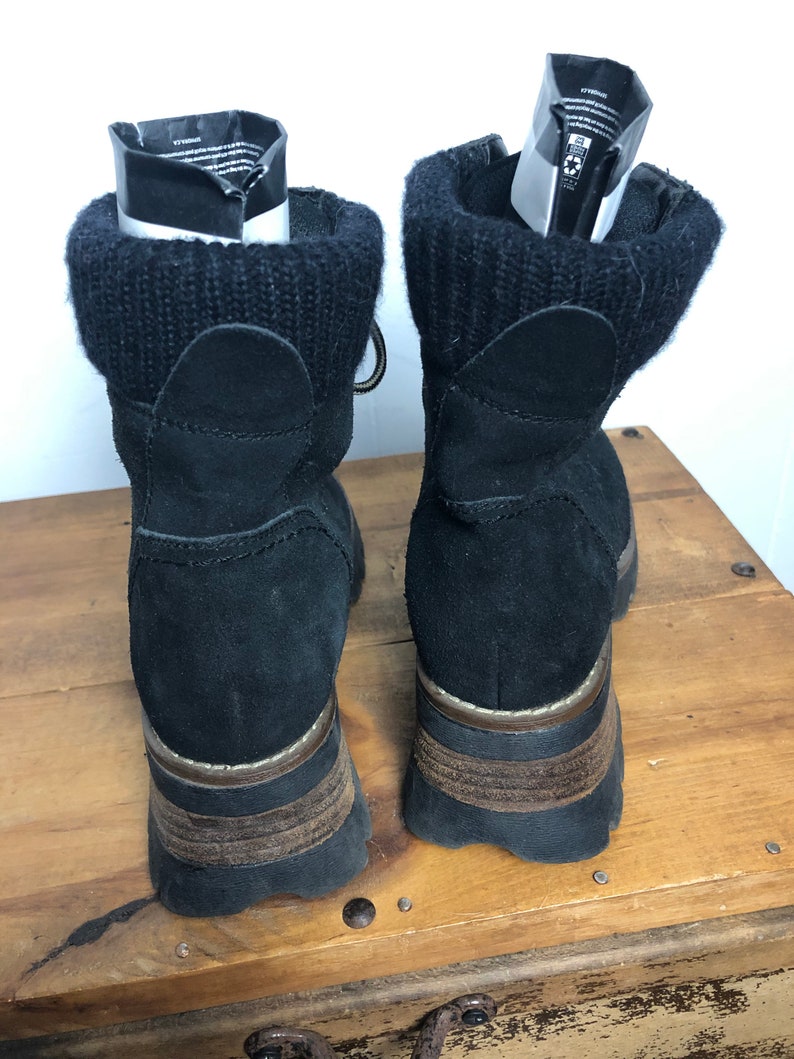 May include: Black suede ankle boots with a chunky platform sole and a knit cuff around the top. The boots have a brown leather trim around the sole.