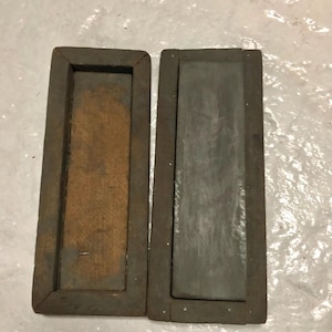 Op de afbeelding: Twee vintage slijpstenen van hout met een donkerbruine afwerking. De stenen zijn rechthoekig en hebben een groef in het midden. De stenen zijn in goede staat en hebben een rustieke uitstraling.