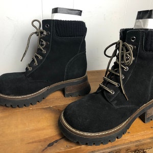 May include: A pair of black suede ankle boots with a chunky platform sole and lace-up closure. The boots have a brown trim around the sole and a black knit cuff at the top.