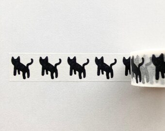 Puede incluir: Un rollo de cinta washi negra y blanca con un patrón repetitivo de siluetas de gatos negros. La cinta está parcialmente desenrollada, revelando el patrón.