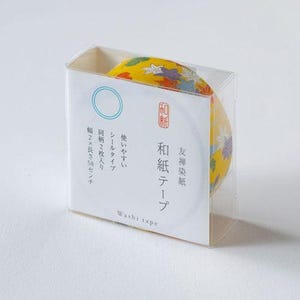 Puede incluir: Un rollo de cinta washi amarilla con un estampado floral, empaquetado en una caja de plástico transparente. La caja tiene texto japonés y una etiqueta blanca con un círculo azul y un sello rojo. La cinta mide aproximadamente 5 cm de ancho.