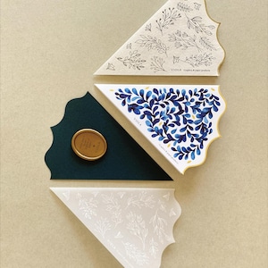 May include: Three triangular paper cones with a floral design. The cones are in different colours: white with white floral design, white with blue floral design, and green with a gold wax seal. The text "VIOLA" is printed on each cone.