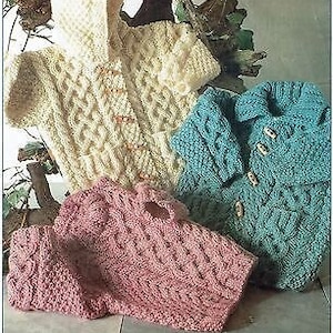 Könnte beinhalten: Drei gestrickte Baby-Pullover in verschiedenen Farben: Creme, Rosa und Blau. Jeder Pullover hat ein Zopfmuster und Knopfverschlüsse.