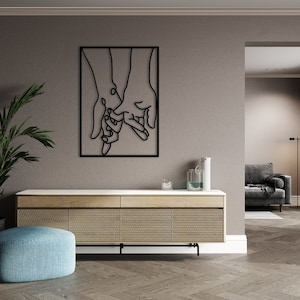 May include: Black metal wall art depicting two hands holding each other. The art is framed and mounted on a light gray wall.