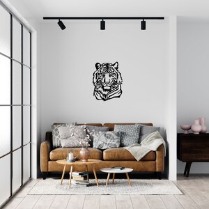 May include: A black and white silhouette of a tiger's head is mounted on a white wall above a brown leather sofa with throw pillows. The sofa is in a living room with a wooden coffee table and a side table.