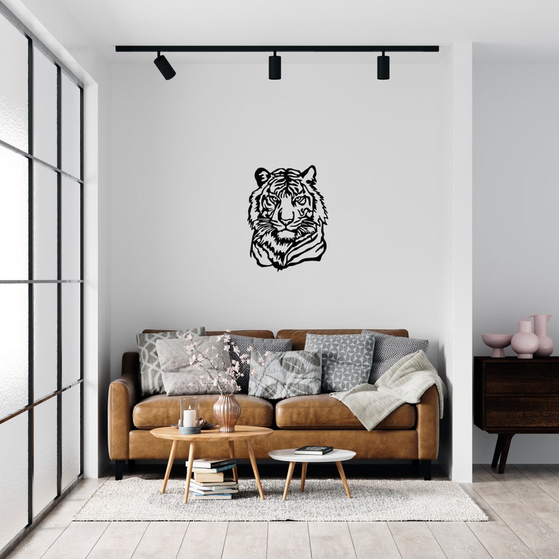 May include: A black and white silhouette of a tiger's head is mounted on a white wall above a brown leather sofa with throw pillows. The sofa is in a living room with a wooden coffee table and a side table.