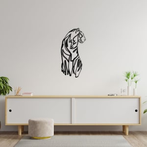 May include: A black and white line art wall decor of a tiger in a sitting pose. The tiger is facing to the right and has a long tail. The decor is mounted on a white wall above a wooden cabinet.