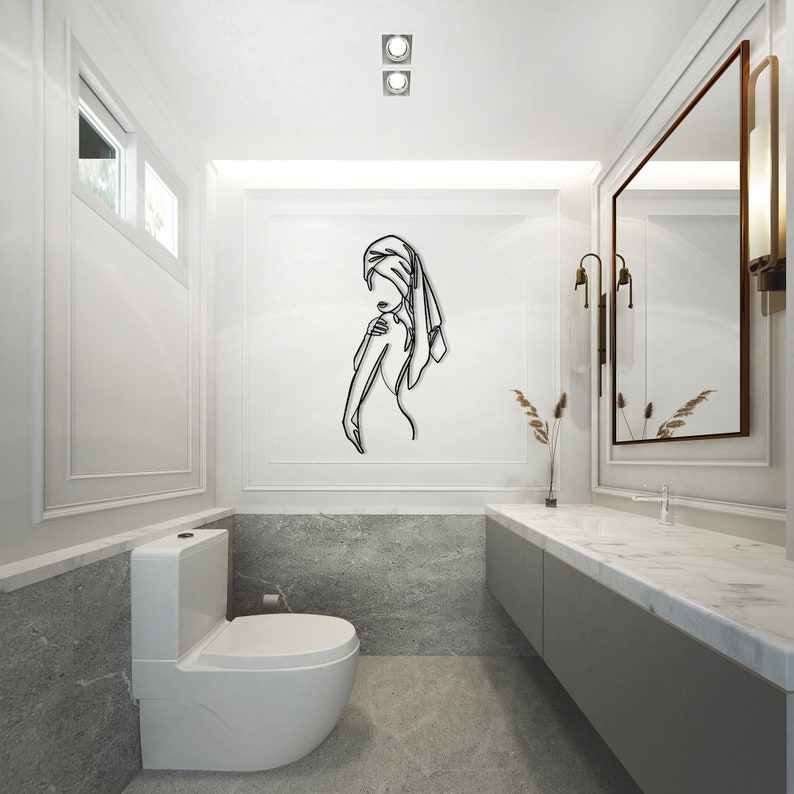 May include: A white bathroom with a toilet, a sink, and a mirror. The mirror is framed in a white frame with gold accents. There is a black metal wall sculpture of a person with a towel on their head.