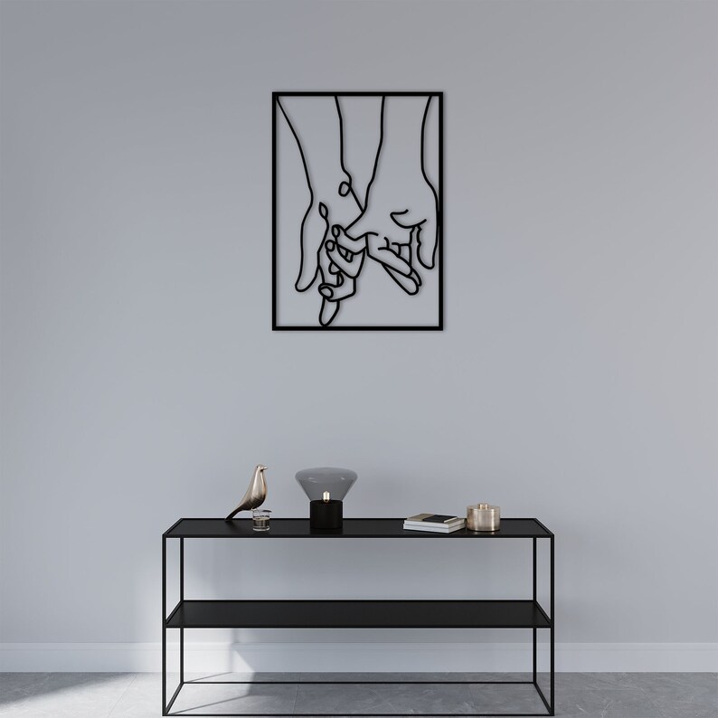 May include: Black metal wall art depicting two hands holding each other. The art is framed in a black square frame.