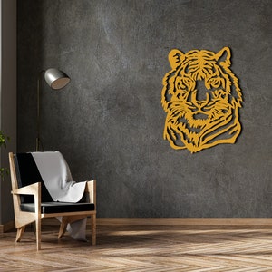 May include: A wooden wall decor featuring a tiger's head in a yellow-gold color. The tiger's head is facing forward with a serious expression. The decor is mounted on a gray textured wall.
