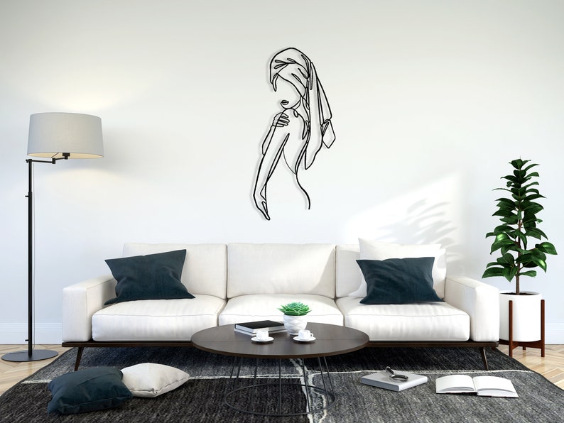 May include: A black metal wall sculpture of a person with a towel wrapped around their head. The sculpture is mounted on a white wall in a living room setting.