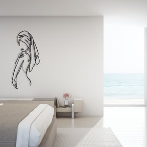May include: A black line art wall decor of a person with a towel wrapped around their head, standing in a minimalist bedroom with a view of the ocean.