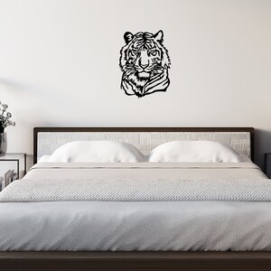 May include: A black and white silhouette of a tiger's head is mounted on a white wall above a bed with white bedding. The bed is in a modern bedroom with white brick walls and a wooden floor.