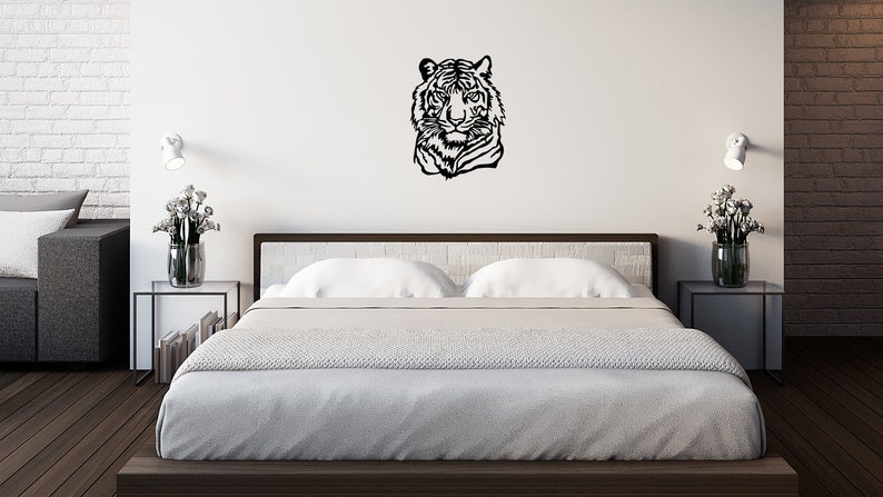 May include: A black and white silhouette of a tiger's head is mounted on a white wall above a bed with white bedding. The bed is in a modern bedroom with white brick walls and a wooden floor.