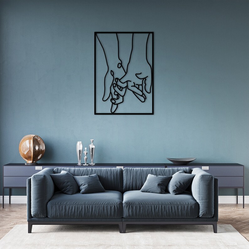 May include: Black metal wall art sculpture of two hands holding each other. The sculpture is framed in a black square.