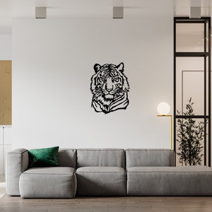 May include: A black metal wall decor featuring a tiger's head silhouette. The decor is mounted on a white wall in a modern living room setting. A gray sofa with a green pillow is in the foreground.