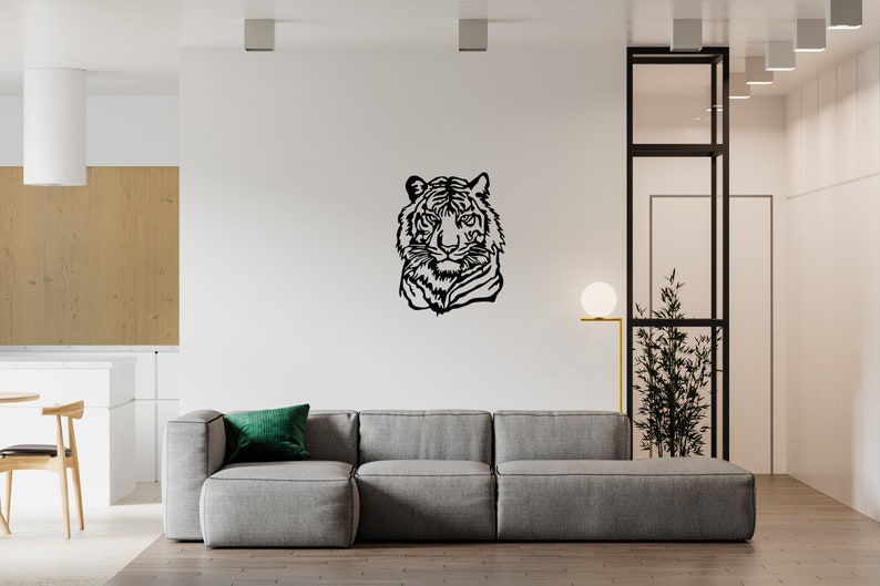 May include: A black metal wall decor featuring a tiger's head silhouette. The decor is mounted on a white wall in a modern living room setting. A gray sofa with a green pillow is in the foreground.