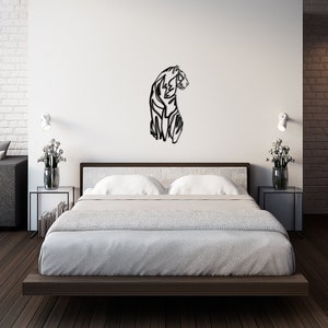 May include: A black metal wall art sculpture of a tiger in a modern bedroom setting. The sculpture is mounted on a white wall above a bed with white bedding and a dark wood frame. The bedroom has a white brick wall, a grey sofa, and a dark wood floor.
