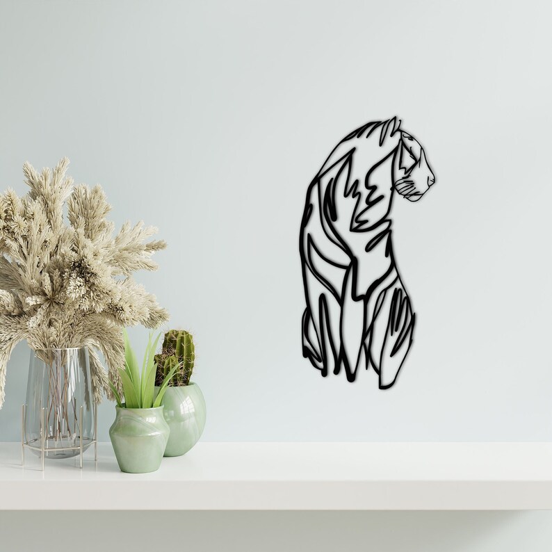 May include: Black metal wall art sculpture of a tiger in a minimalist line art style. The tiger is facing to the right and is in a curled position.