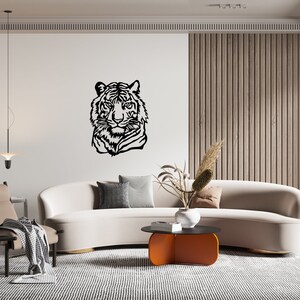 May include: A white curved sofa with a black and white tiger head silhouette wall decor, a brown armchair, a coffee table with an orange top, and a potted plant with dried flowers.