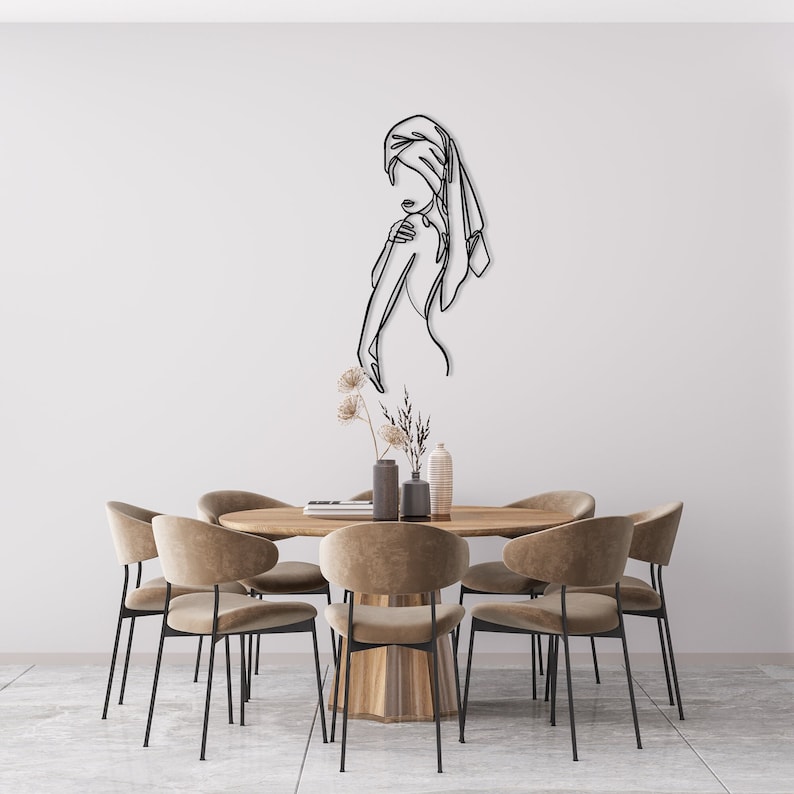 May include: A black metal wall art sculpture depicting a woman with a towel wrapped around her head. The sculpture is hanging above a wooden dining table with six brown chairs.