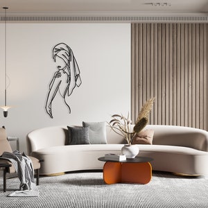 May include: A white curved sofa with a black metal coffee table and a black and white patterned rug. The coffee table has a unique orange base. A black line art drawing of a person with a towel on their head is on the wall behind the sofa.