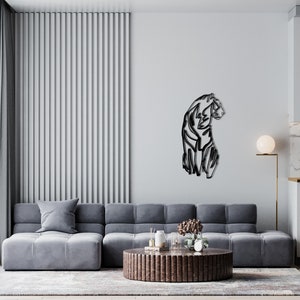 May include: A black metal wall sculpture of a stylised panther sitting on a white wall in a modern living room. The sculpture is in the centre of the wall and is surrounded by a grey sectional sofa, a coffee table, and a floor lamp.