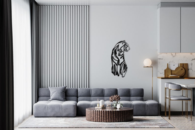 May include: A black metal wall sculpture of a stylised panther sitting on a white wall in a modern living room. The sculpture is in the centre of the wall and is surrounded by a grey sectional sofa, a coffee table, and a floor lamp.