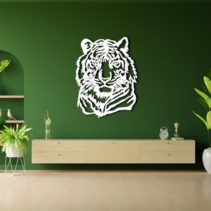 May include: White wooden wall decor featuring a tiger head silhouette against a green wall. The decor is displayed above a light wood cabinet with two drawers. There are potted plants on either side of the cabinet.