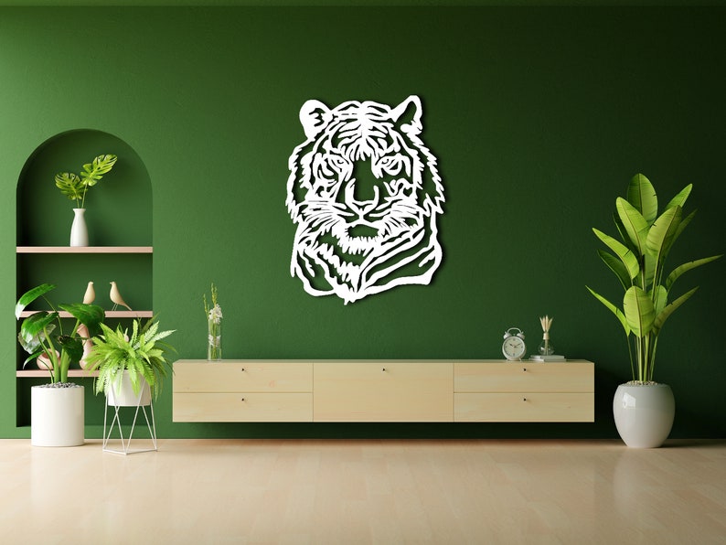 May include: White wooden wall decor featuring a tiger head silhouette against a green wall. The decor is displayed above a light wood cabinet with two drawers. There are potted plants on either side of the cabinet.