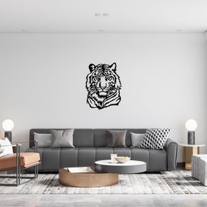 May include: A black and white silhouette of a tiger's head is displayed on a white wall in a living room. The room features a gray sofa, a brown coffee table, and a brown leather armchair.