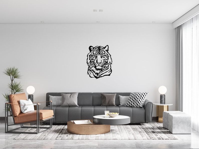 May include: A black and white silhouette of a tiger's head is displayed on a white wall in a living room. The room features a gray sofa, a brown coffee table, and a brown leather armchair.