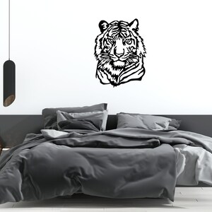 May include: Black and white silhouette of a tiger's head on a white wall above a gray bed with white bedding.