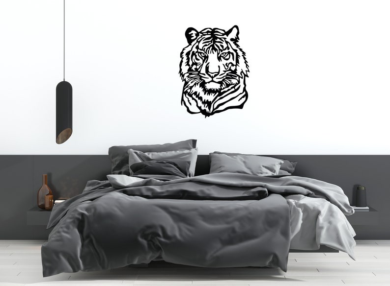 May include: Black and white silhouette of a tiger's head on a white wall above a gray bed with white bedding.
