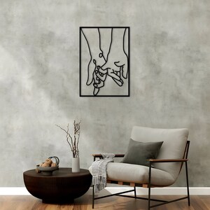 May include: Black metal wall art depicting two hands holding each other. The hands are outlined in black and are set against a white background.