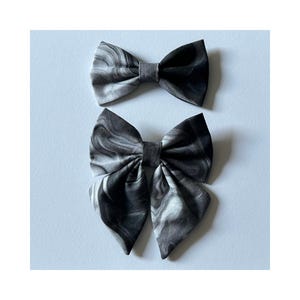 May include: Two black and white marbled fabric hair bows. The larger bow is tied in a classic bow shape, while the smaller bow is tied in a more modern, asymmetrical style.