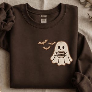 May include: A dark brown crewneck sweatshirt featuring a DTG printed graphic of a light-coloured ghost holding a mug with the word COFFEE printed on it, accompanied by three small flying bats. The text NO EMBROIDERY ONLY DTG PRINTING is visible.