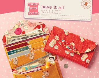 May include: A yellow and orange fabric wallet with a floral pattern. The wallet is open and has cash, credit cards, and other items inside. The wallet is on a pink background with white polka dots. The text "have it all WALLET" is visible in the image.