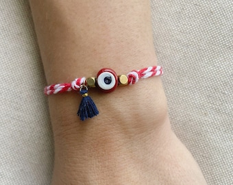 Puede incluir: Pulsera de cuerda roja y blanca con un amuleto de ojo azul y un borla azul.