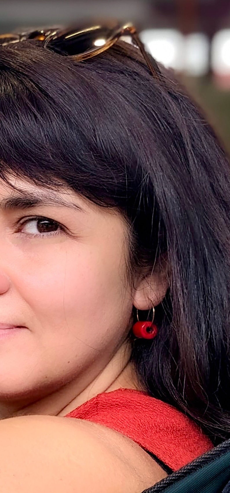 K&ouml;nnte beinhalten: Eine Frau mit langen dunklen Haaren, die ein rotes Oberteil und rote Creolen tr&auml;gt.