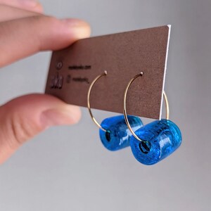 K&ouml;nnte beinhalten: Ein Paar goldene Creolen mit einer leuchtend blauen Glasperle an jedem Creolen.