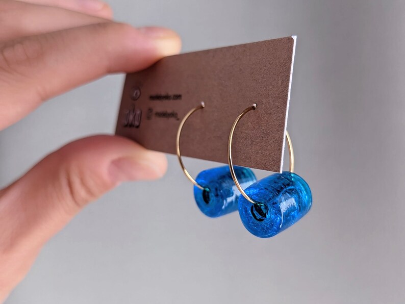 K&ouml;nnte beinhalten: Ein Paar goldene Creolen mit einer leuchtend blauen Glasperle an jedem Creolen.